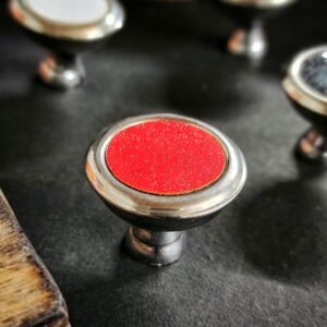 Round metallic cabinet knob with a glossy red center, placed on a dark background.