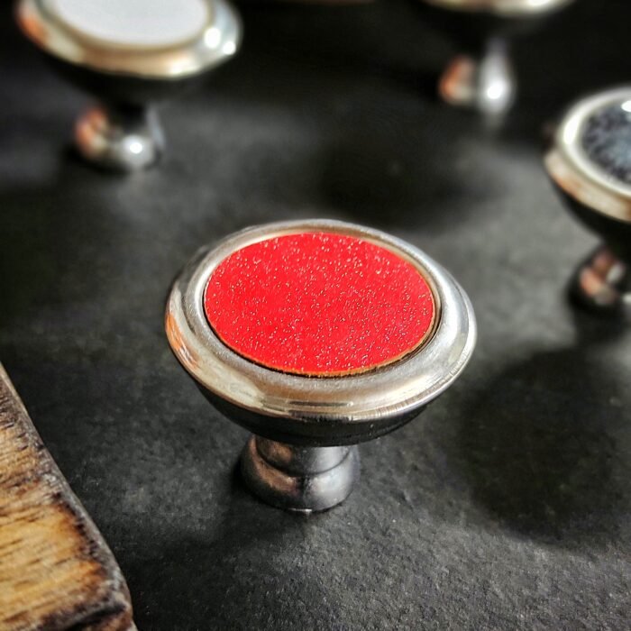 1 (2) Round metallic cabinet knob with a glossy red center, placed on a dark background.