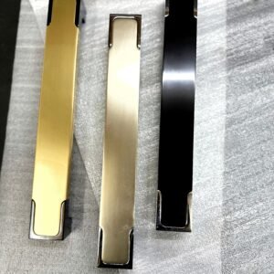 Three modern square-edge cabinet pull handles in gold, silver, and black finish placed on a textured surface.