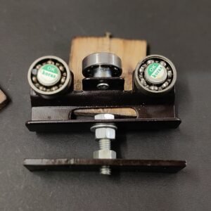 Heavy-duty sliding gate roller assembly with three ball-bearing wheels mounted on a black metal base and wooden support blocks