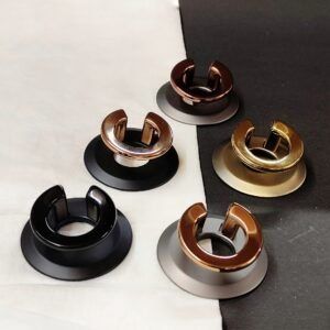 Set of five metallic door stoppers in different finishes – black, bronze, copper, gold, and chrome – displayed on a fabric and dark background.