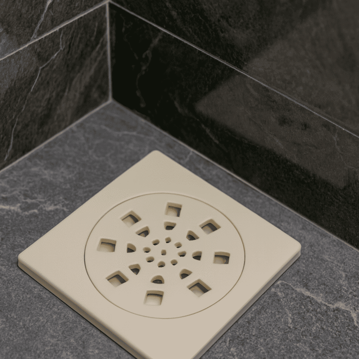 White plastic floor drain with circular decorative cover featuring radial oval and central round holes, installed on textured tiles with water flow.