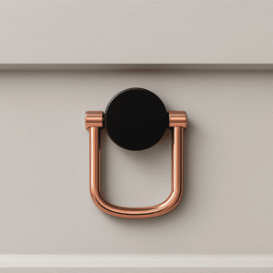 Modern U-shaped drawer pull handle with a round black base plate in rose-gold finish, mounted on a light-colored cabinet drawer.